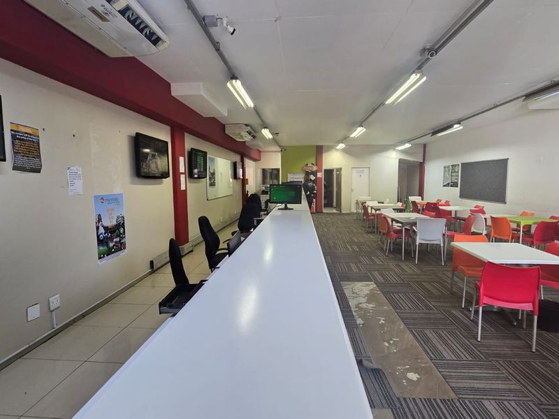 Open-plan commercial space featuring a long service counter, tiled and carpeted flooring, and overhead fluorescent lighting, suitable for a betting shop or office.
