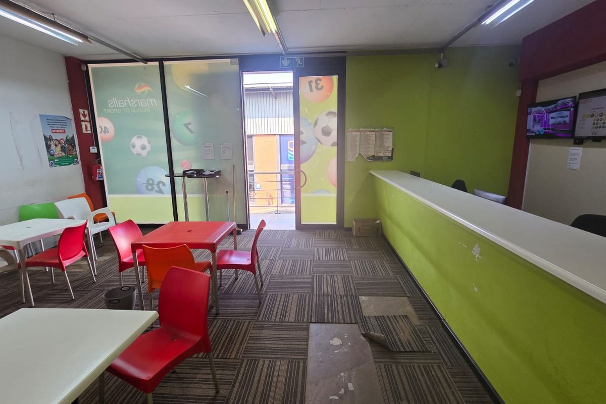 Open plan commercial space featuring a built-in service counter, carpet tile flooring, and fluorescent lighting, suitable for a betting shop or retail office.