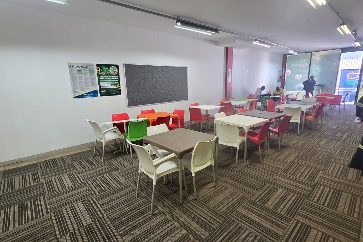 Open-plan commercial space featuring patterned carpet tiles, track lighting, and a glass entrance, suitable for a betting shop or casual seating area.