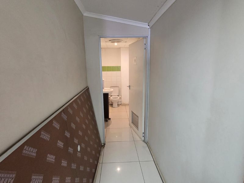 A narrow hallway with tiled flooring leading to a bathroom, featuring plain walls and standard door access.