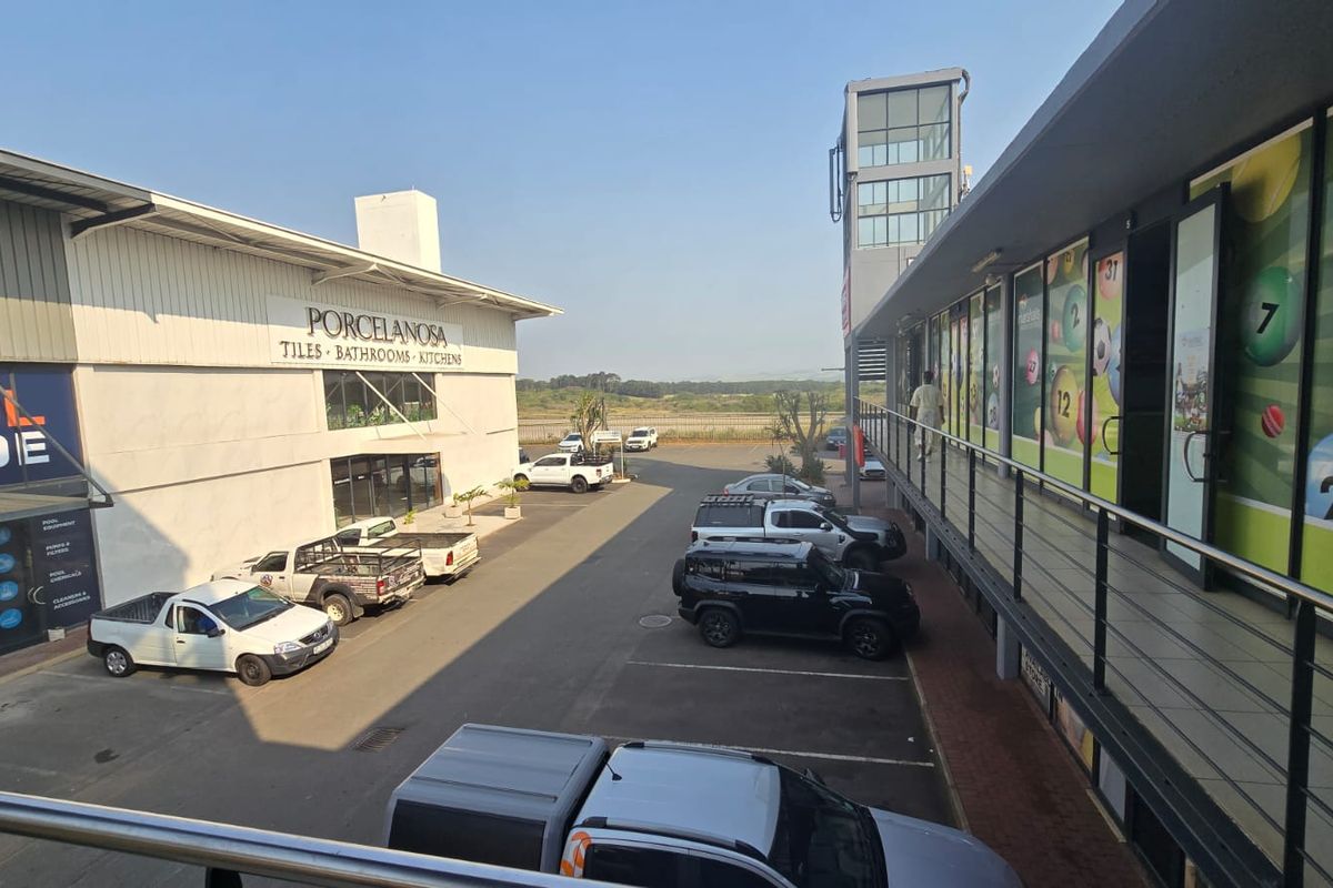 An elevated view of a commercial property complex featuring a paved parking area, metal-clad warehouse building, and a multi-level retail storefront.