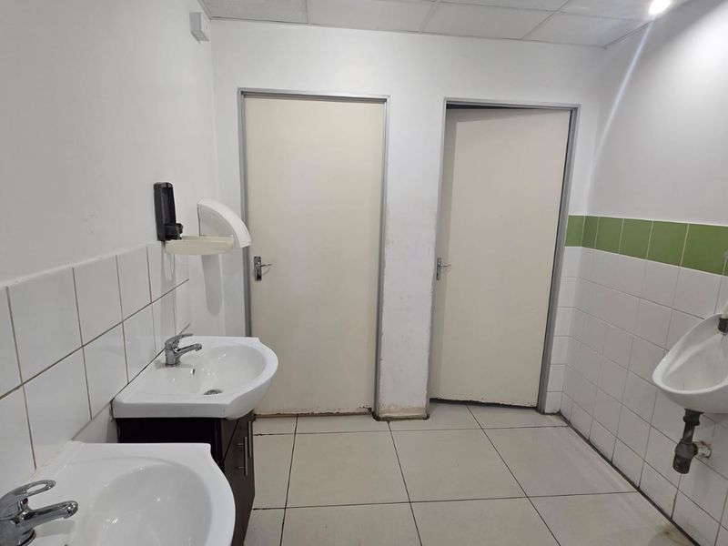 Commercial bathroom facility featuring dual pedestal washbasins, a wall-mounted urinal, and tiled surfaces throughout.