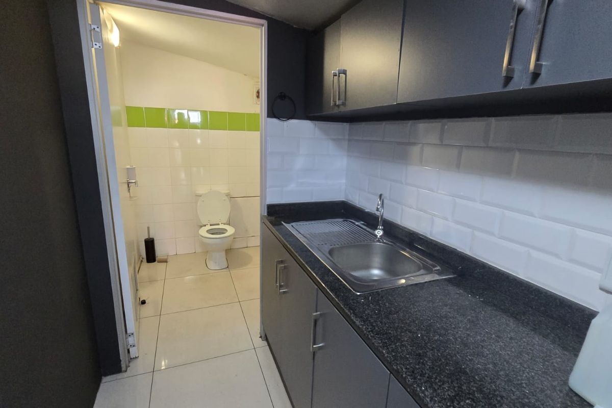 A compact kitchenette featuring dark cabinetry, granite countertops, and a subway tile backsplash, with an adjacent private restroom facility.