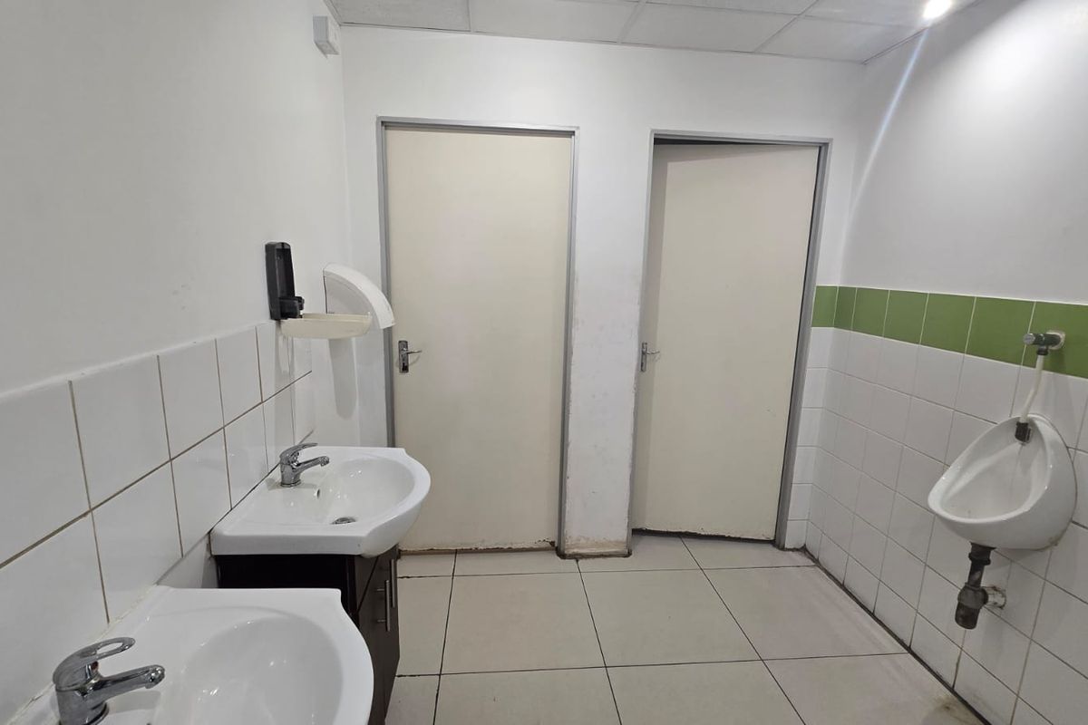 Commercial bathroom facility featuring dual pedestal washbasins, a wall-mounted urinal, and tiled surfaces throughout.