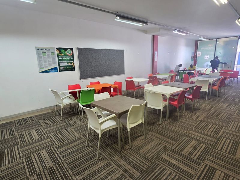Open-plan commercial space featuring patterned carpet tiles, track lighting, and a glass entrance, suitable for a betting shop or casual seating area.