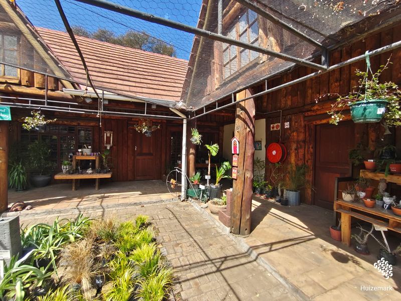 A rustic outdoor courtyard area featuring timber-clad walls, paved flooring, and a protective overhead netting structure, suitable for retail or garden display use.