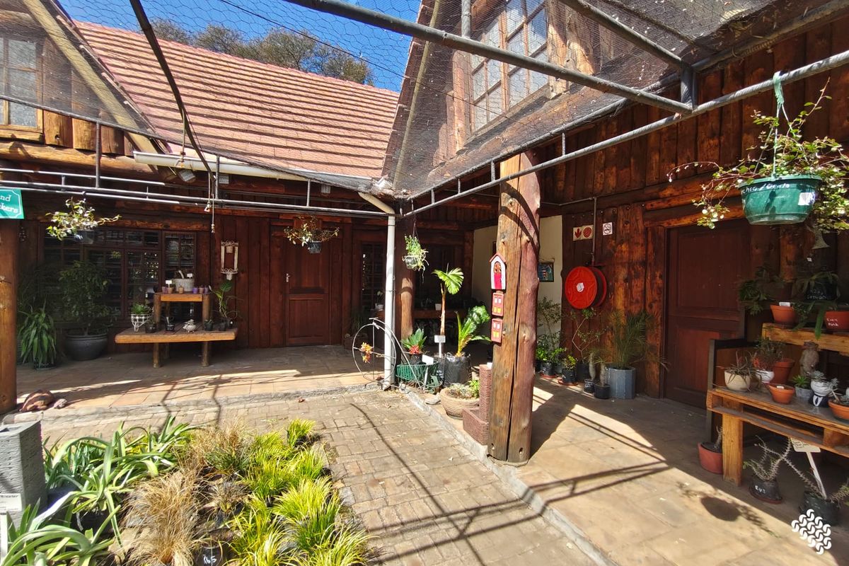 A rustic outdoor courtyard area featuring timber-clad walls, paved flooring, and a protective overhead netting structure, suitable for retail or garden display use.