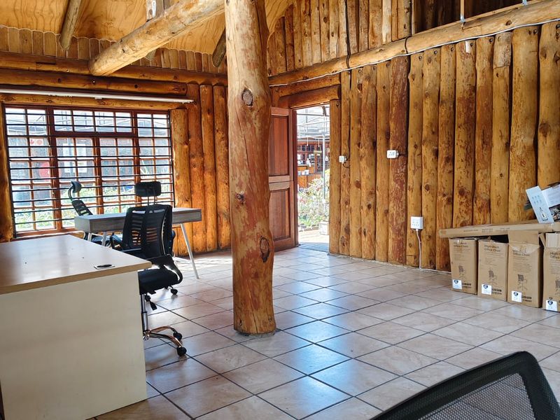 Rustic office space featuring exposed timber log walls, vaulted timber ceiling, ceramic tiled flooring, and a large central timber support column.
