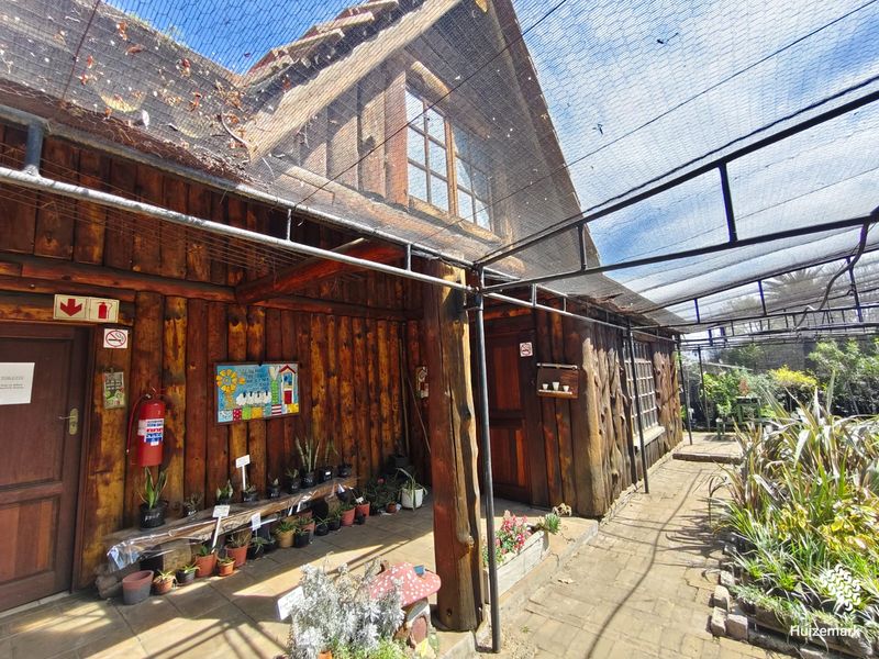 Rustic log cabin style retail exterior featuring a covered walkway with shade netting and timber construction.