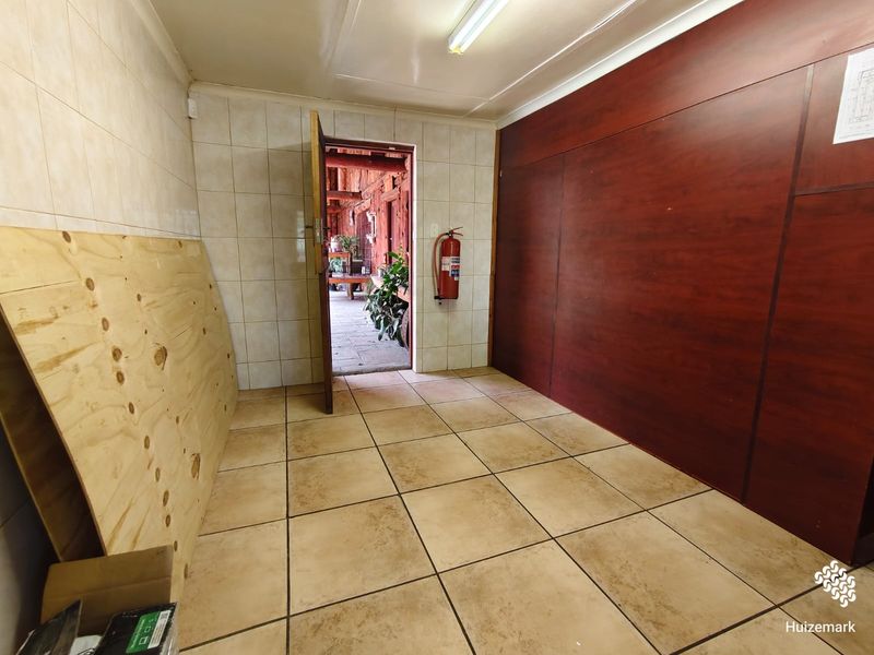 A vacant utility space featuring tiled flooring, tiled wall sections, and a mounted fire extinguisher, providing direct access to an outdoor area.