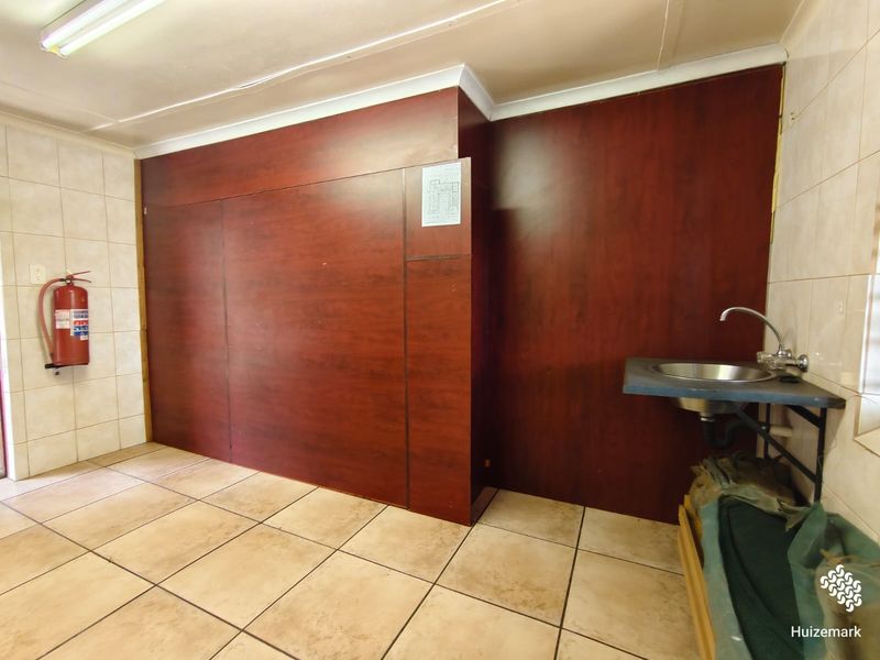 A functional utility space featuring tiled flooring, a wall-mounted sink, and wood-look paneling, suitable for various commercial or storage purposes.