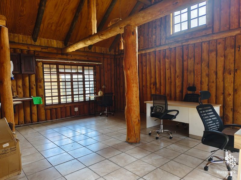 Rustic office space featuring log cabin walls, exposed timber beams, vaulted ceilings, and large grid-pattern windows with tiled flooring.