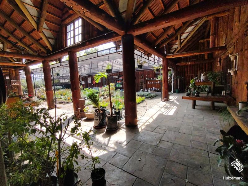 Spacious covered outdoor retail area featuring rustic timber log columns, exposed wooden roof trusses, and durable tiled flooring, ideal for a nursery or garden center.