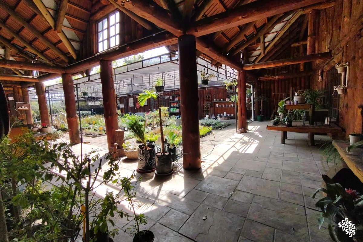 Spacious covered outdoor retail area featuring rustic timber log columns, exposed wooden roof trusses, and durable tiled flooring, ideal for a nursery or garden center.