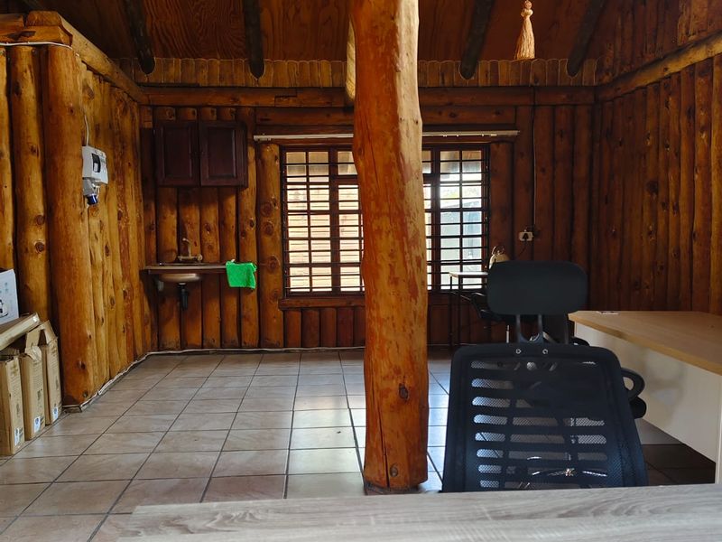 Rustic office space featuring log walls, exposed timber ceiling beams, tiled flooring, and a built-in wall-mounted sink.