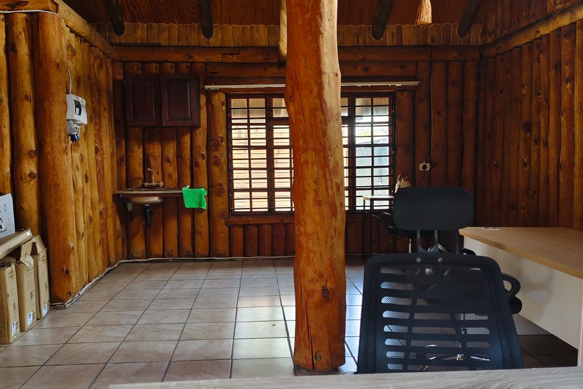 Rustic office space featuring log walls, exposed timber ceiling beams, tiled flooring, and a built-in wall-mounted sink.
