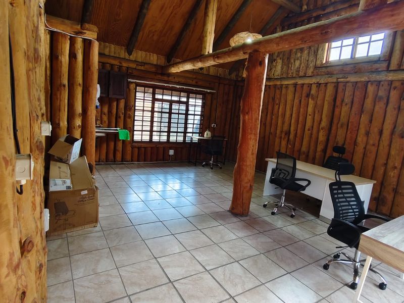 Rustic office space featuring exposed log walls, timber roof beams, and tiled flooring, providing a unique character-filled workspace.
