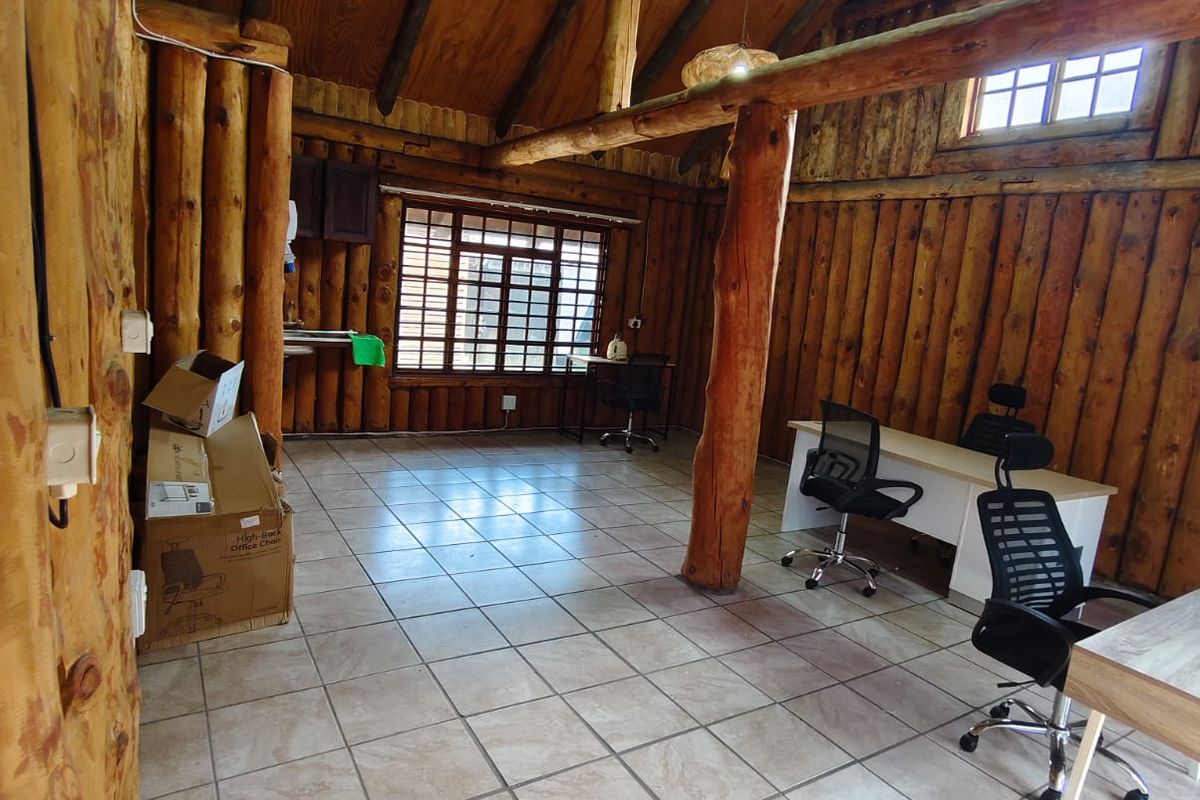 Rustic office space featuring exposed log walls, timber roof beams, and tiled flooring, providing a unique character-filled workspace.