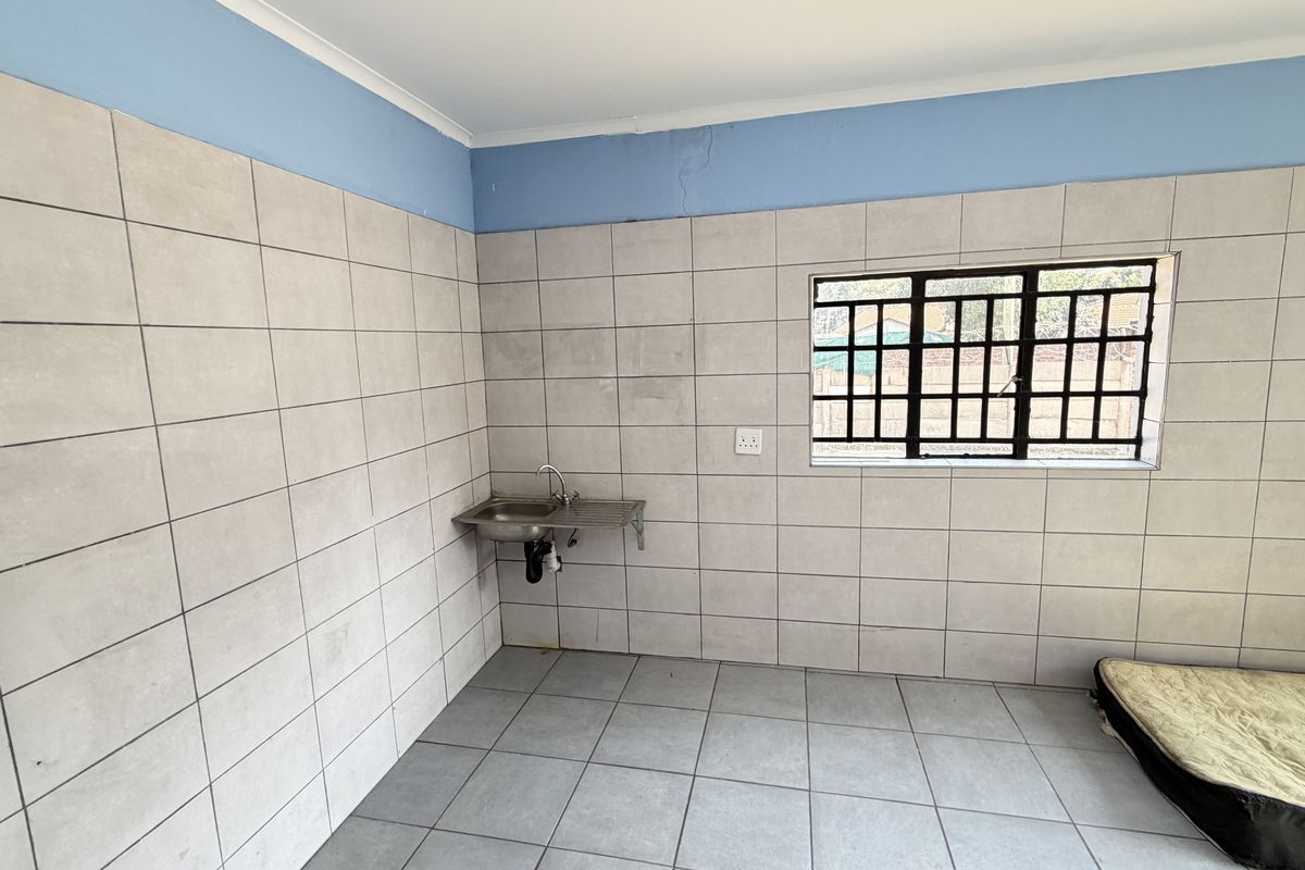 A basic utility kitchen area featuring tiled walls, a stainless steel sink, and a window with security bars.
