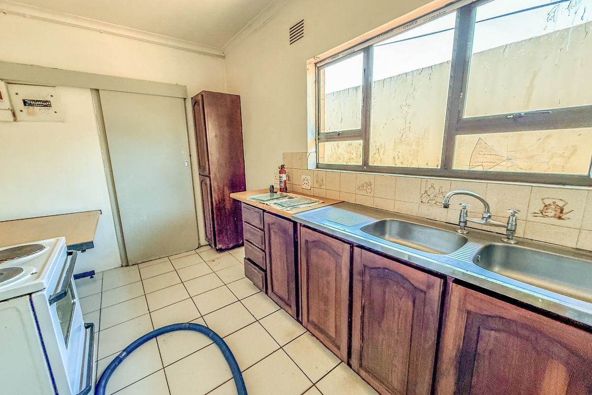 A functional kitchen featuring wooden cabinetry, a double stainless steel sink, and tiled flooring, requiring some maintenance and cosmetic updates.