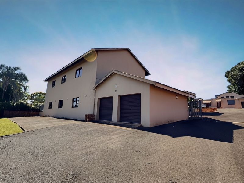 Exterior view of a commercial property featuring a double garage, paved driveway, and plastered facade under a clear sky.