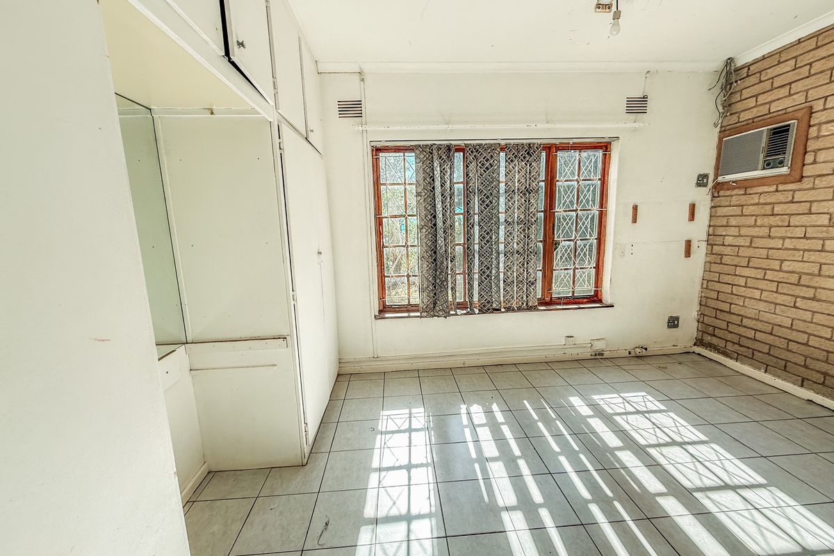 An empty bedroom featuring tiled flooring, built-in cupboards, an exposed brick feature wall, and a wall-mounted air conditioning unit.