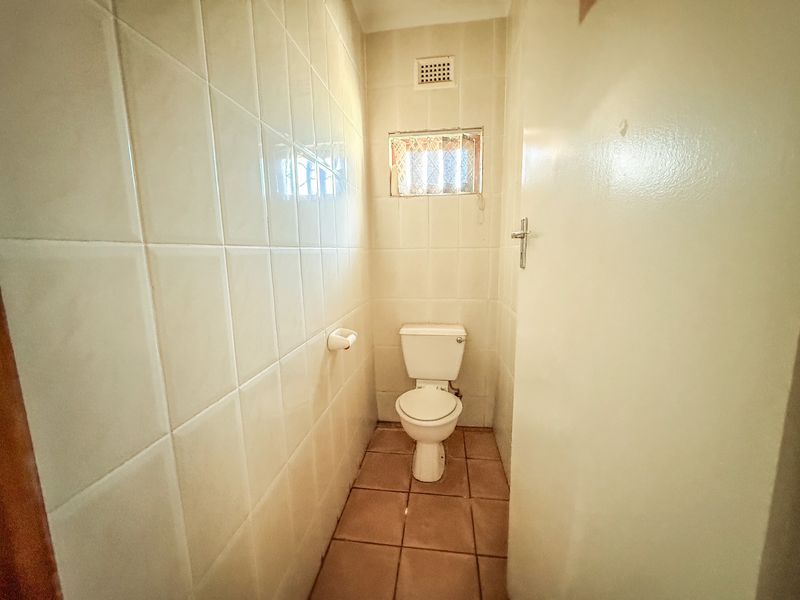 A compact, functional guest bathroom featuring full-height ceramic wall tiling, tiled flooring, and a standard toilet suite.
