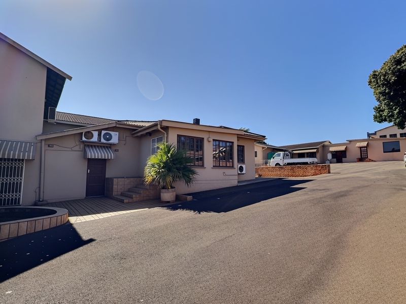 Exterior view of a commercial property featuring an asphalt driveway, multiple building sections, and external air conditioning units.