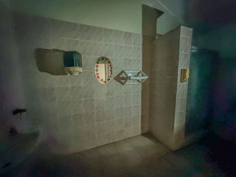 A dimly lit, dated bathroom featuring tiled walls and flooring with a built-in shower partition wall.
