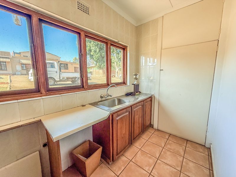 A functional scullery area featuring a stainless steel sink, wooden cabinetry, tiled backsplash, and tiled flooring, offering practical utility space.