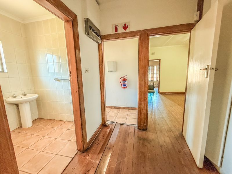A functional commercial hallway featuring tiled and wooden flooring, a pedestal basin, and essential fire safety equipment with access to adjacent rooms.