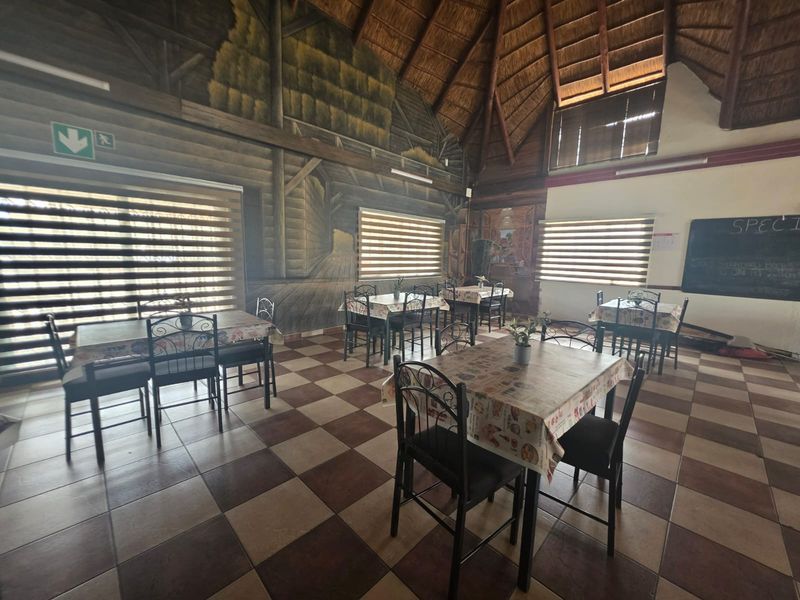 Spacious dining area featuring a high thatched roof with exposed timber trusses and checkered tiled flooring, creating a rustic restaurant atmosphere.