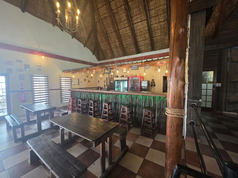A rustic bar area featuring a high thatched ceiling, timber support beams, a built-in bar counter, and tiled flooring.