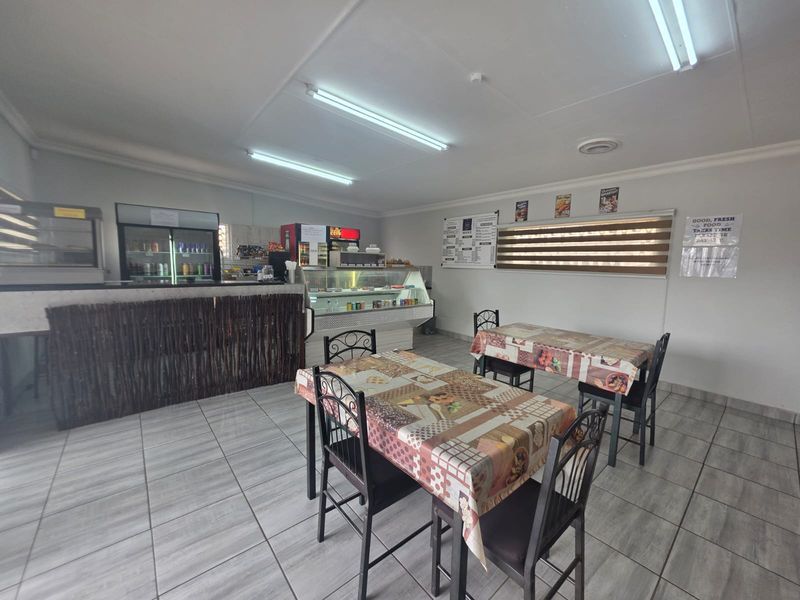 Open-plan restaurant dining area featuring tiled flooring, fluorescent lighting, and a service counter with integrated display refrigeration units.