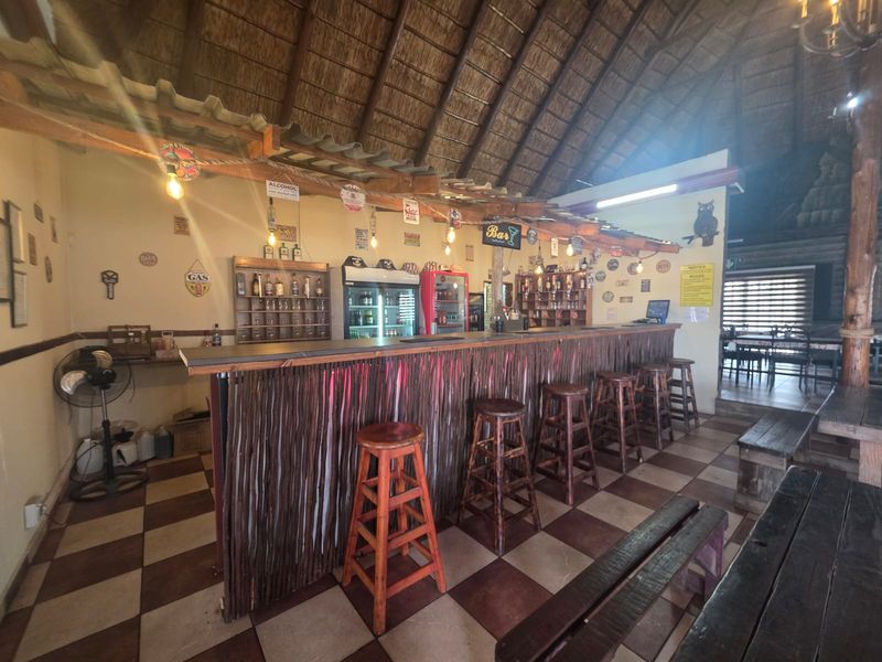 A rustic bar area featuring a built-in counter, traditional thatched roofing, and tiled flooring, creating a casual atmosphere for a restaurant setting.