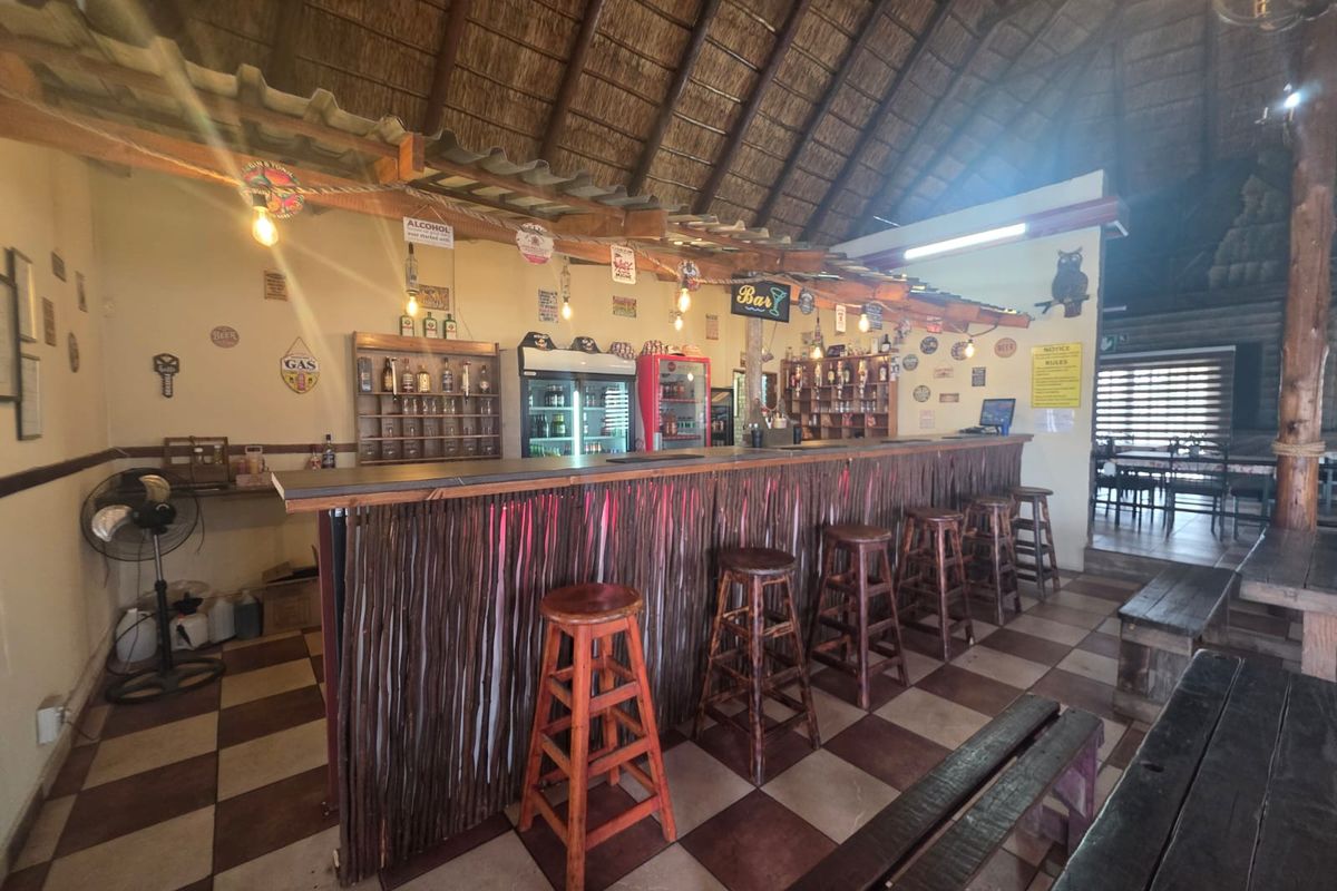 A rustic bar area featuring a built-in counter, traditional thatched roofing, and tiled flooring, creating a casual atmosphere for a restaurant setting.