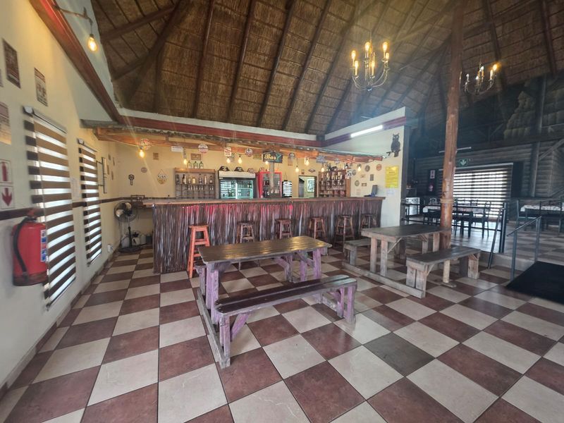 Spacious restaurant bar area featuring a high thatched ceiling, checkered tile flooring, and a central built-in bar counter with integrated lighting.
