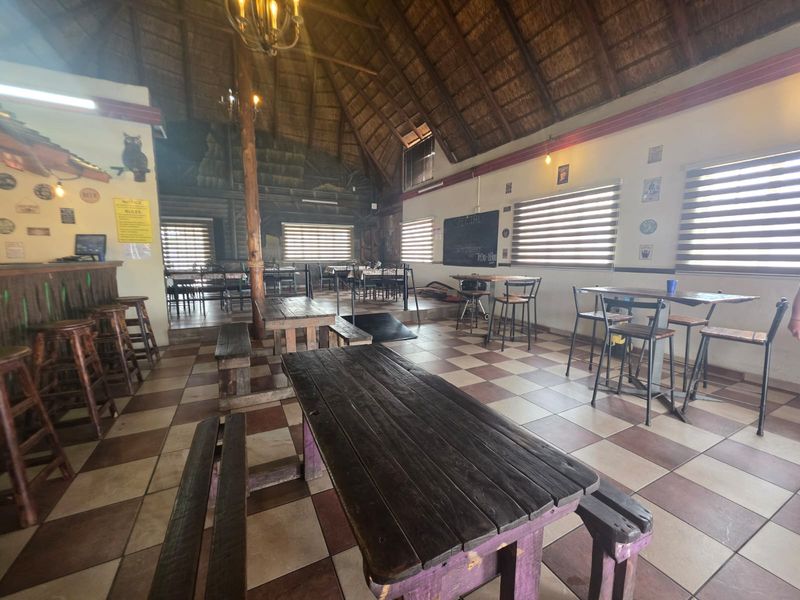 Spacious open-plan restaurant area featuring a high thatched roof, exposed timber support, and tiled flooring with a built-in bar counter.