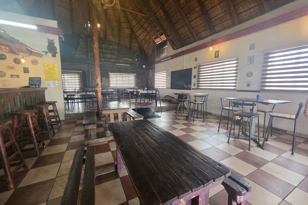Spacious open-plan restaurant area featuring a high thatched roof, exposed timber support, and tiled flooring with a built-in bar counter.