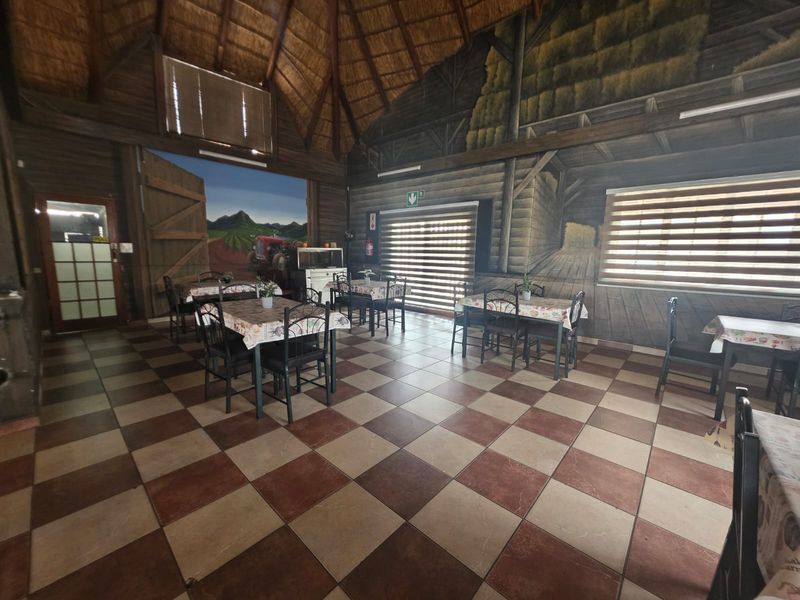 Spacious dining area featuring a high thatched roof with exposed timber beams, ceramic tiled flooring, and large windows with roller blinds.