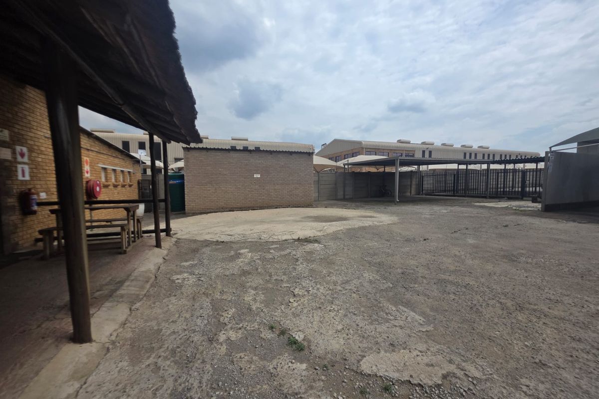 Rear exterior area of the restaurant featuring a covered patio section, brick structures, and a large paved parking or utility yard.