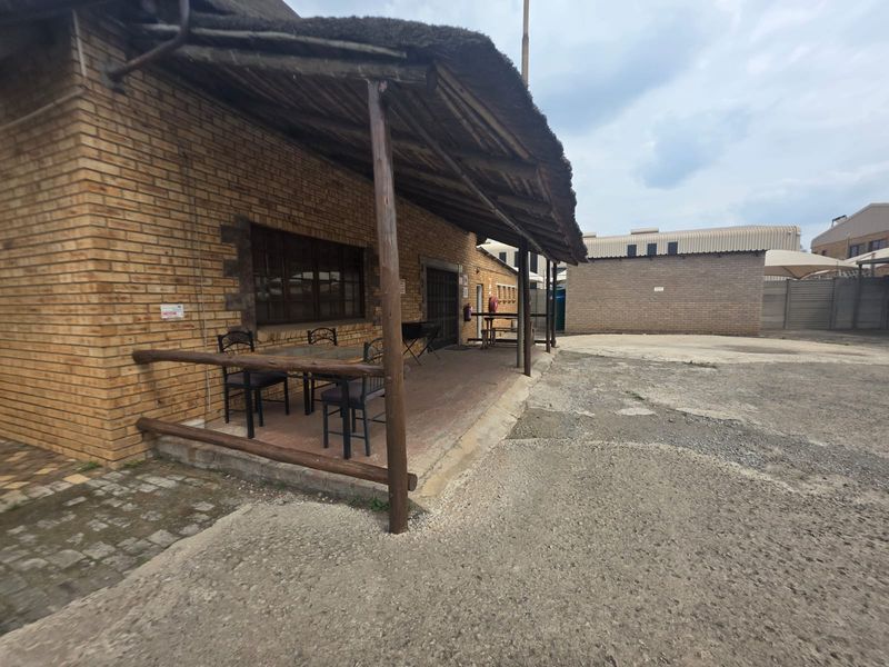 A covered outdoor patio area featuring a traditional thatched roof, brick exterior walls, and tiled flooring, providing a rustic seating space.