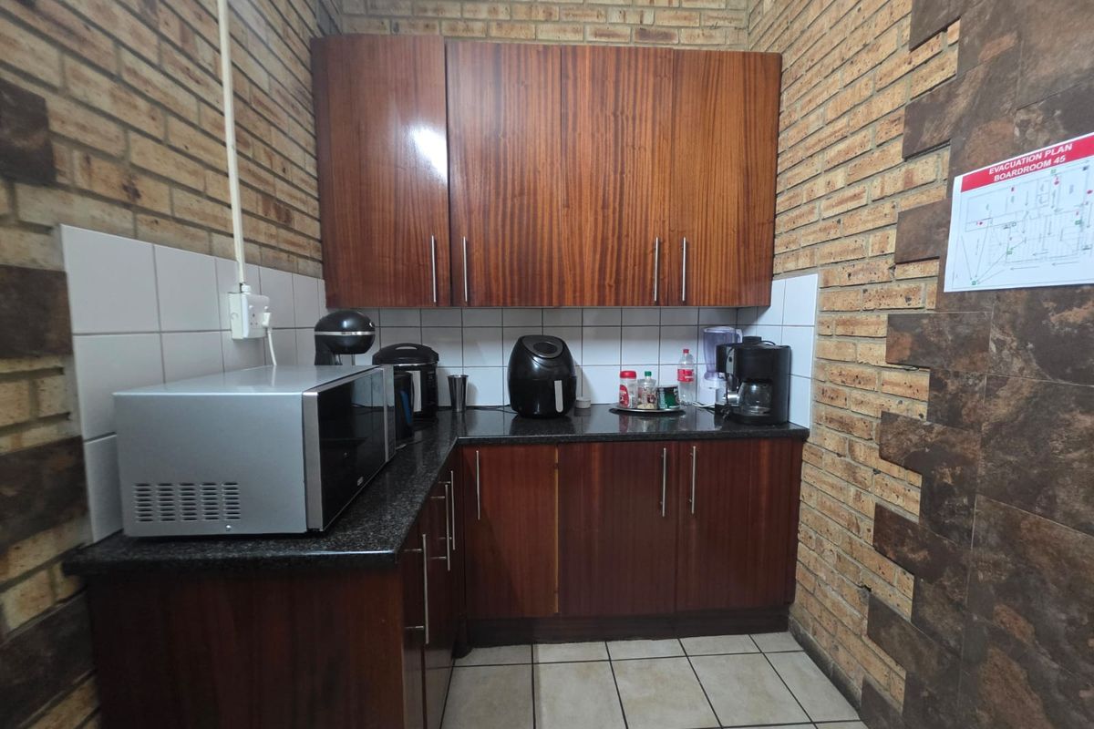 A compact kitchen area featuring dark wood-look cabinetry, granite countertops, tiled backsplash, and exposed brick walls with ceramic floor tiling.