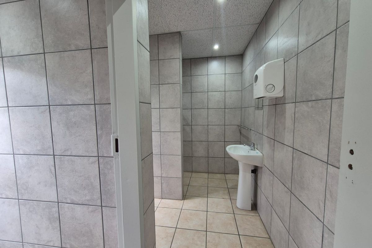 A functional office bathroom featuring full-height wall tiling, a pedestal sink, and recessed ceiling lighting.