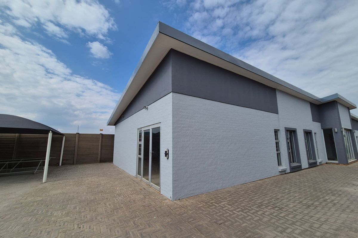 Rear exterior view of the office building featuring modern grey painted brickwork, aluminium window frames, sliding doors, and a paved courtyard area with shade port.