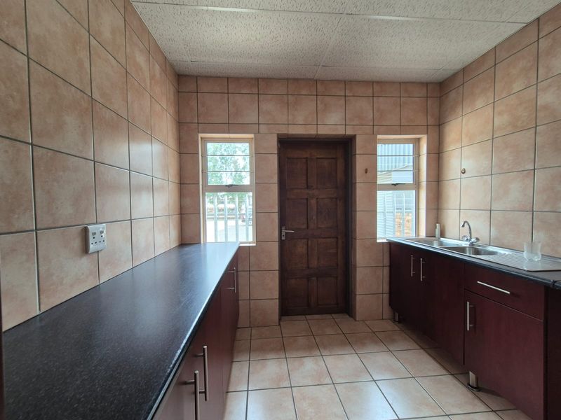 A functional scullery or utility area featuring tiled walls and floors, built-in cabinetry with laminate countertops, and a stainless steel sink.