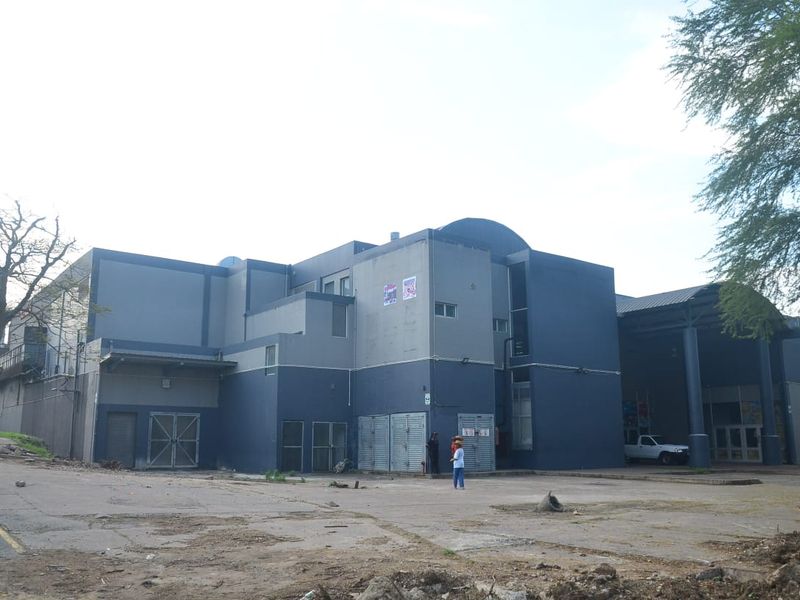 Exterior view of a commercial building featuring a multi-level facade, covered loading area, and paved driveway access.