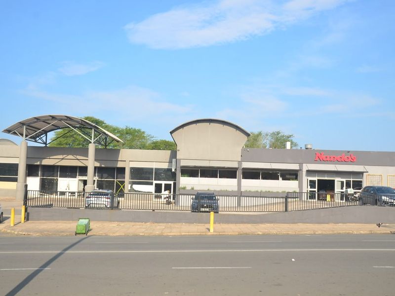 Front exterior view of a commercial building featuring modern architectural roof structures, large glass storefronts, and secure perimeter fencing.