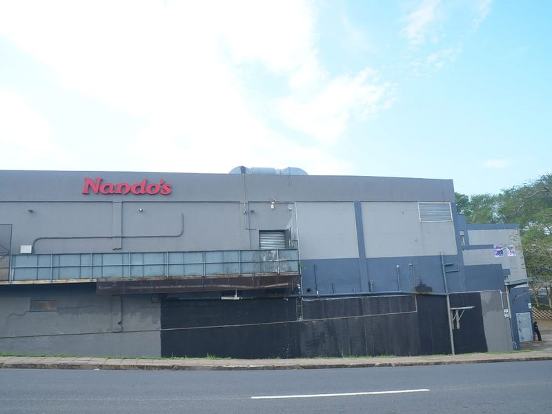 Exterior view of a commercial building facade featuring prominent signage, metal railings, and ventilation infrastructure along a street frontage.