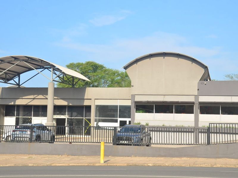Front exterior view of a commercial building featuring a modern metal roof structure, large glass windows, and secure perimeter fencing with paved parking.